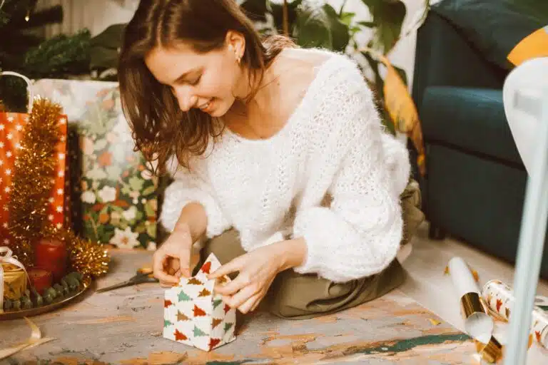 young woman wrapping christmas gift in decorative paper