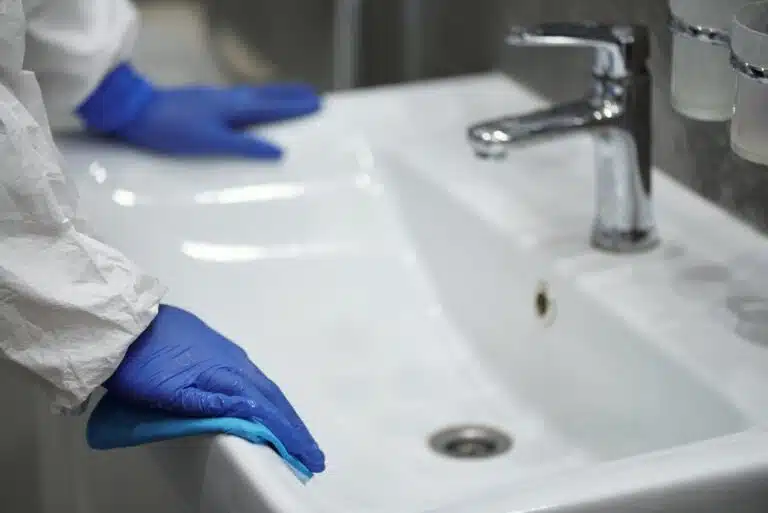 person in latex gloves cleaning washbasin